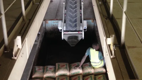 Ein Mann ist damit beschäftigt, mit Unterstützung eines halbautomatischen Beladesystems befüllte Zementsäcke auf eine offene Ladefläche zu packen.