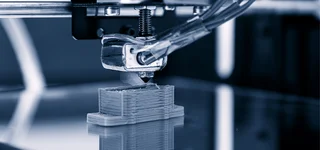 Nahaufnahme eines 3D-Druckers beim Schmelzschichtverfahren, druckt präzise ein Bauteil aus Kunststoffschichten auf einer glatten Bauplattform.