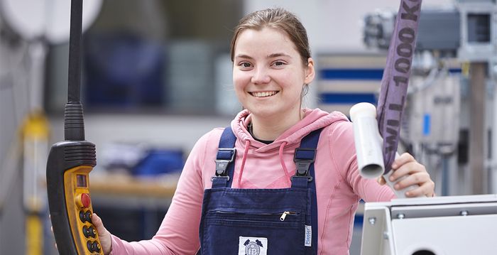 Eine Auszubildende steht in der Produktionshalle und bedient eine Maschine.