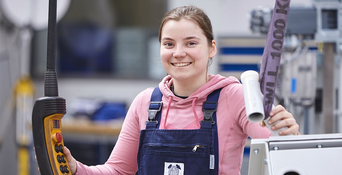 Eine Auszubildende steht in der Produktionshalle und bedient eine Maschine.