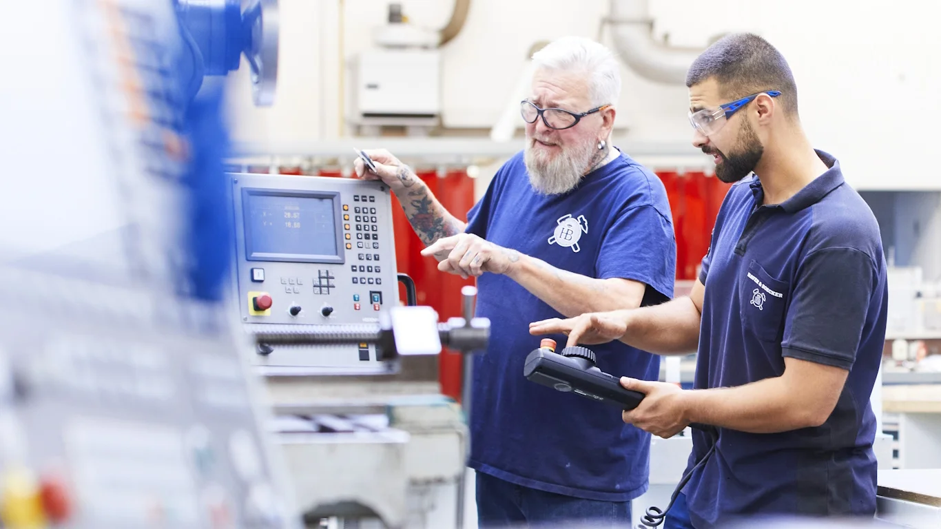 Zwei Männer in Arbeitskleidung bedienen gemeinsam eine CNC-Maschine bei einer Schulung in der Haver & Boecker Academy.