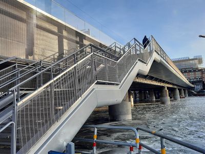 Pont de chemin de fer avec escalier piétonnier en avant-plan et parapets en métal tissé 