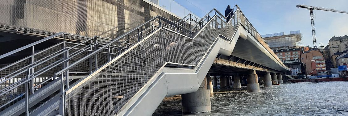 Pont de chemin de fer avec escalier piétonnier en avant-plan et parapets en métal tissé 