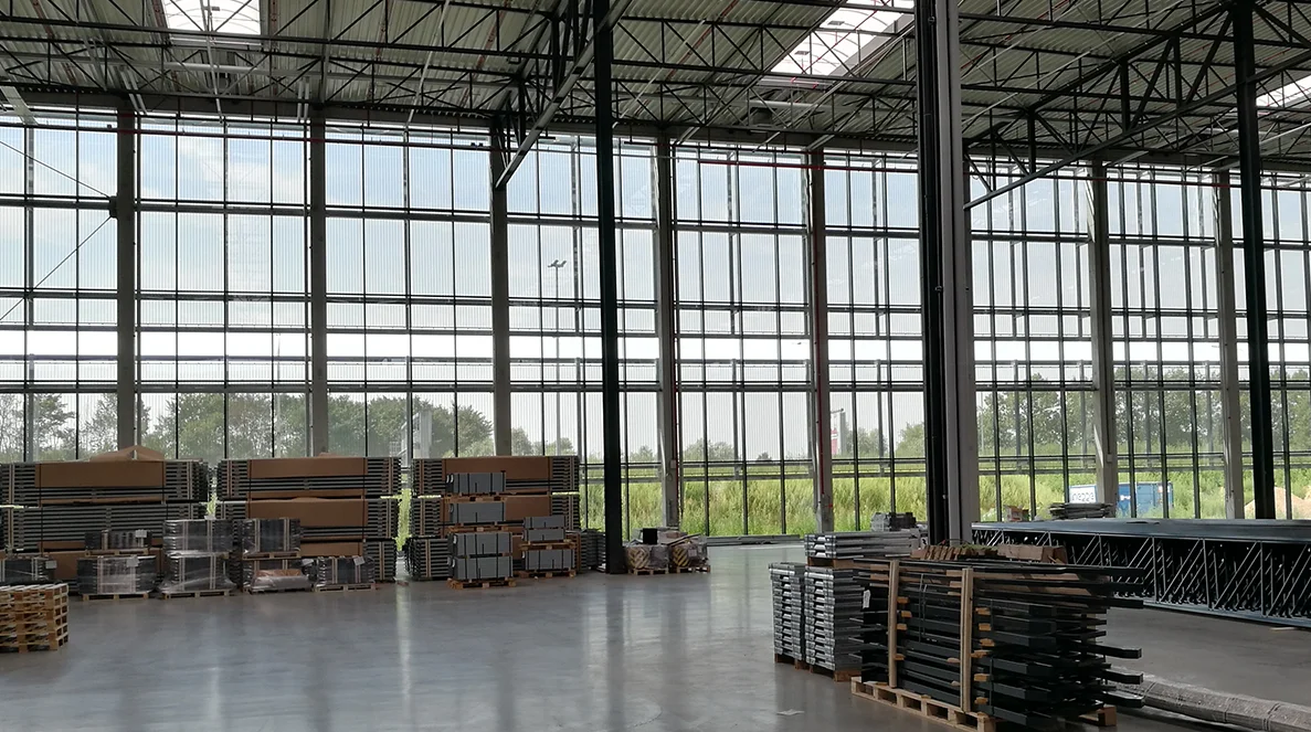 Vue intérieure à travers une façade en tissu métallique architecturale semi-transparente offrant une vue dégagée sur les champs environnants et le ciel