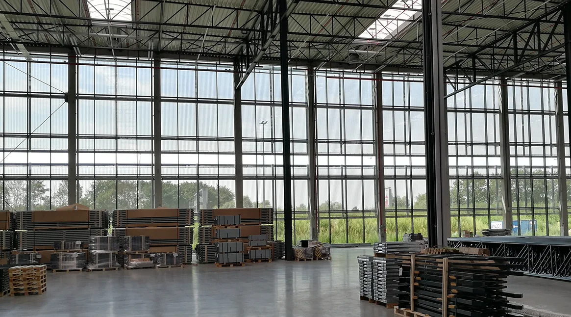 Interior view through a semi-transparent architectural mesh façade with a clear view of the surrounding fields and the sky
