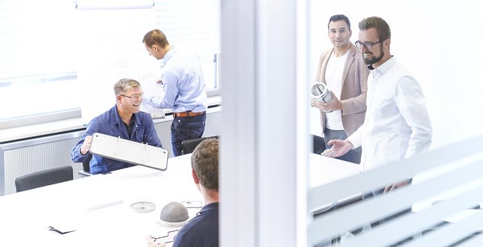 Ein Meeting mit fünf Personen, alle besprechen sich auf Augenhöhe.