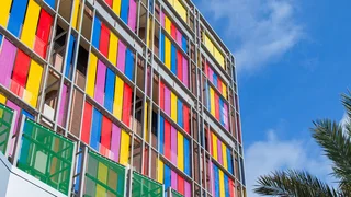 Colourful wire mesh façade consisting of yellow, blue, red and pink painted stainless steel meshes.