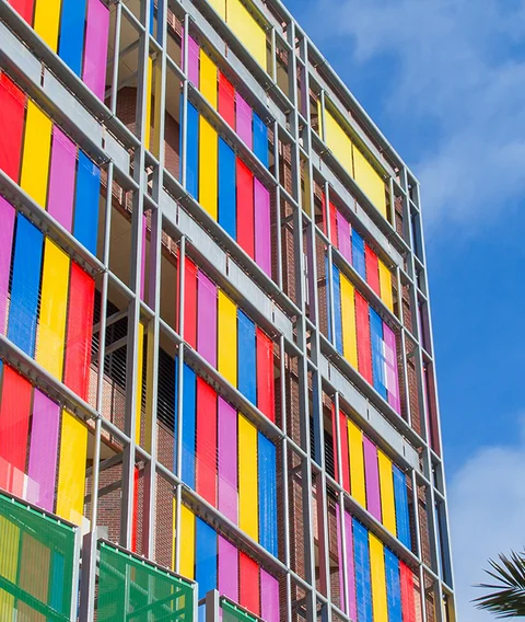 Bunte Drahtgewebefassade, bestehend aus gelb, blau, rot und rosa lackierten Edelstahlgeweben.