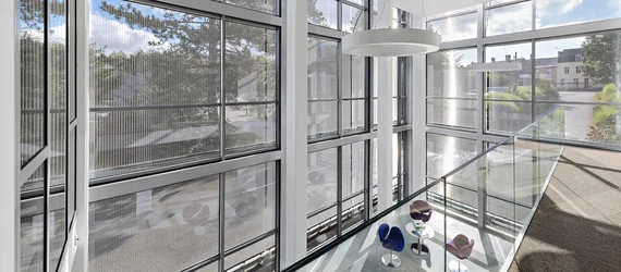 Light-filled interior with an expansive glass façade and architectural mesh solar shading, creating a modern lounge environment with comfortable seating and natural daylight.