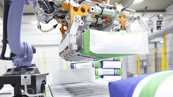 A blue robot palletizer lifts filled bags from the assembly line with its gripper arm. 