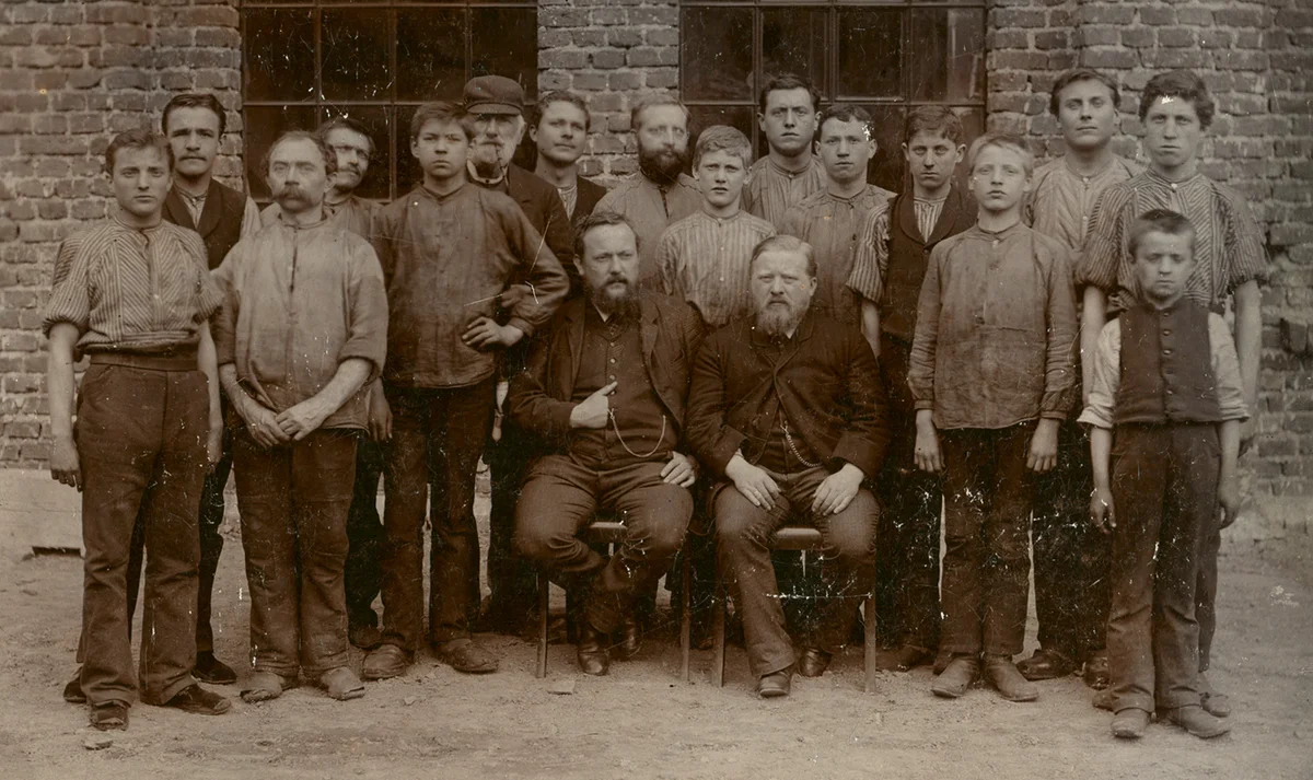 Photo historique montrant les fondateurs de l’entreprise avec leurs collaborateurs devant le bâtiment de l’entreprise