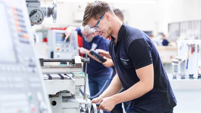 Teilnehmer eines Lehrgangs für Drehen und Fräsen beim Arbeiten an einer Drehmaschine