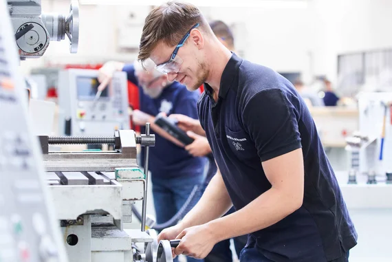 Teilnehmer eines Lehrgangs für Drehen und Fräsen beim Arbeiten an einer Drehmaschine