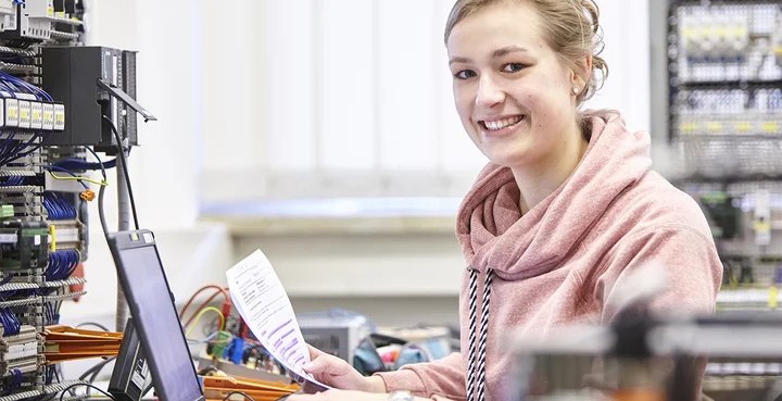 Eine duale Studentin sitzt am Laptop  vor einem Schaltschrank.