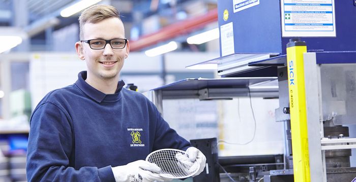 Ein Auszubildender hält ein selbst hergestelltes Teil stolz vor sich.