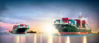 Zwei mit Containern beladene Frachtschiffe bei Sonnenaufgang im Hafen, Symbol für Ballastwasseraufbereitung und globalen Warenverkehr.