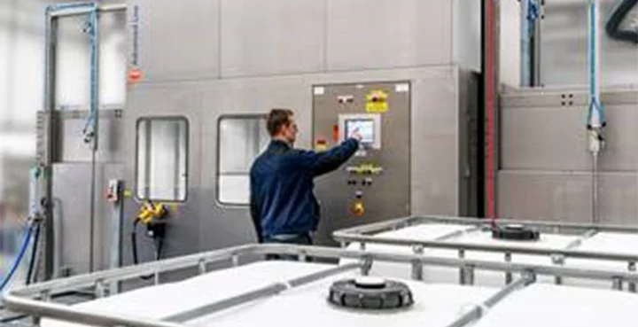 Ein Mann in einer blauen Jacke stellt an dem Kontollbildschirm die Abfüllanlage für flüssige Produkte ein. Neben ihm stehen IBC-Tanks.