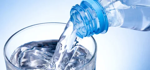 Klares Wasser wird aus einer Plastikflasche in ein Glas gegossen, Symbolbild für sauberes Trinkwasser und Wasserwirtschaft.