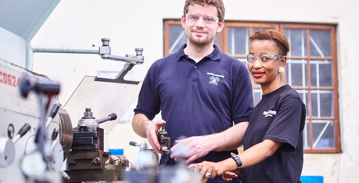 Ein Mann und eine Frau stehen in einer Werkstatt an einer Maschine.
