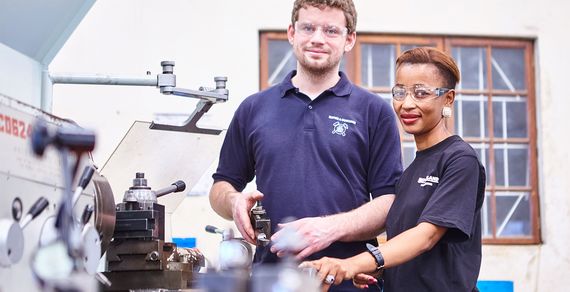 Ein Mann und eine Frau stehen in einer Werkstatt an einer Maschine.