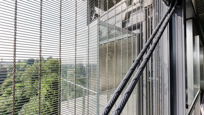 Vue sur les arbres à travers une balustrade semi-transparente en acier inoxydable.