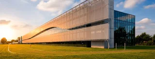 Modernes Bürogebäude mit semitransparenter Metallgewebe-Fassade als Sonnenschutz (LARGO-TWIST), im warmen Abendlicht auf grüner Wiese