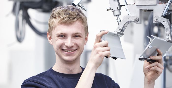 Ein angehender Mechatroniker steht an einer Maschine und überprüft seine Arbeit.