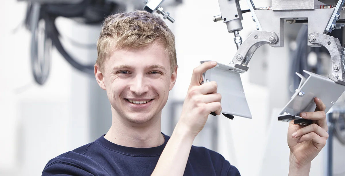 Ein angehender Mechatroniker steht an einer Maschine und überprüft seine Arbeit.
