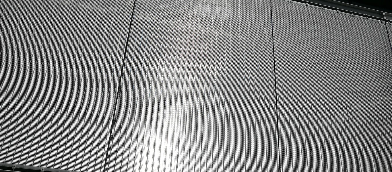 A detailed architectural mesh cladding system serves as a semi-transparent solution for both visual screening and sun protection, combining functionality, transparency, and aesthetic appeal.