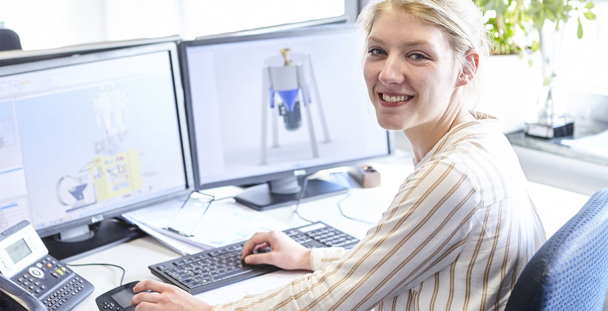 Eine junge Frau sitzt am Computer und arbeitet mit technischen Systemen.