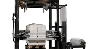 Ein vollautomatischer Palettenstretcher zieht eine Folienhaube über eine befüllte Palette mit Zementsäcken.