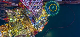 Luftaufnahme einer beleuchteten Offshore-Bohrplattform mit Helikopterlandeplatz zur Aufbereitung von Bohrflüssigkeiten auf offener See.