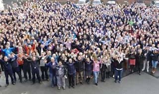 Ein Gruppenbild unserer Mitarbeiterinnen und Mitarbeiter winkend auf dem Hof.