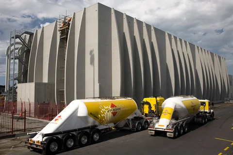 An einer Zement-Flachlagerhalle mit einem besonderen architektonischen Design fahren zwei Silo-LKWs vor.