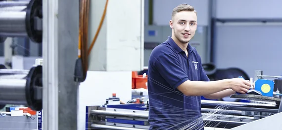 Ein Auszubildender der Drahtweberei zieht einzelne Drähte in die Anlage hinein. 