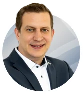 Portrait photo of Mr. Alsmann, smiling, wearing a dark suit with a white shirt, in front of a grey‑blue background, for Haver & Boecker.