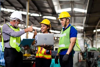Drei Personen in Schutzbekleidung stehen an Laptop und strecken lächelnd die Daumen hoch.