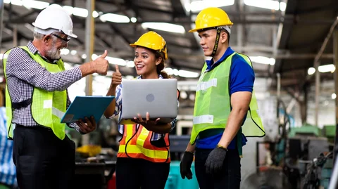 Three people in protective clothing standing at the laptop and giving a smiling thumbs-up.