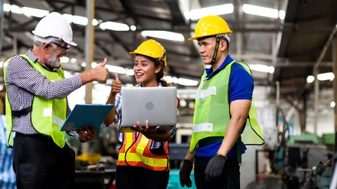 Drei Personen in Schutzbekleidung stehen an Laptop und strecken lächelnd die Daumen hoch.