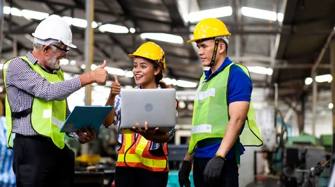 Drei Personen in Schutzbekleidung stehen an Laptop und strecken lächelnd die Daumen hoch.