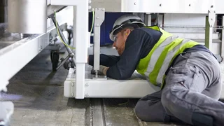 A man with safety helmet and high-visibility vest mounting something, lying under a machine