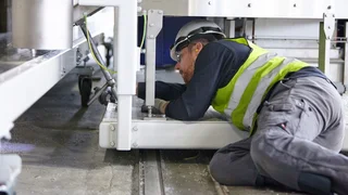 Man with safety helmet and high-visibility vest mounting something, lying under a machine.
