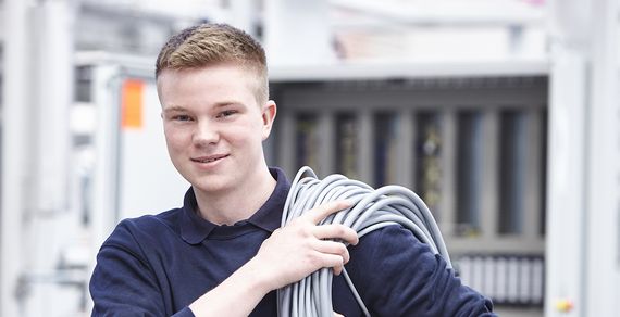 Ein Auszubildender trägt ein langes Kabel über die Schulter gewickelt zu seinem Arbeitsplatz.
