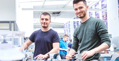 Zwei Auszubildende stehen in der  Lehrwerkstatt an ihrer Werkbank.