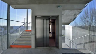 Stair tower with elevator and fall protection made of architectural mesh by Haver & Boecker on a modern exterior facade in daylight.