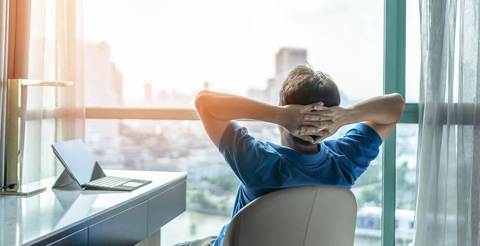 Ein Mann sitzt gelassen in seinem Schreibtischstuhl und schaut aus seinem Bürofenster in den Himmel.