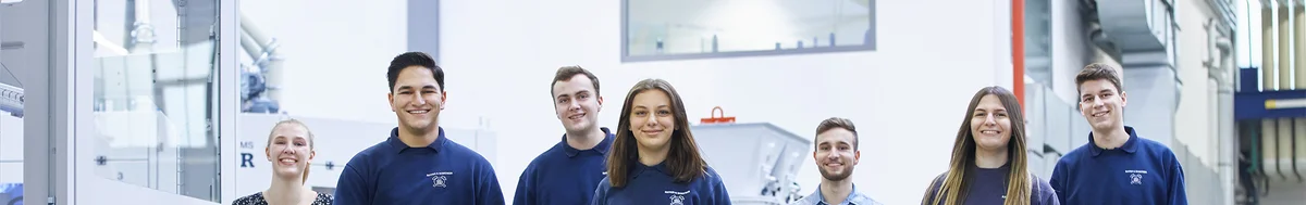 Sieben Auszubildende laufen glücklich durch die Produktionshallen. 