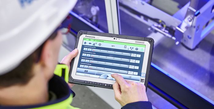 Eine Person mit Schutzkleidung arbeitet mit einem Tablet an einer Maschine.